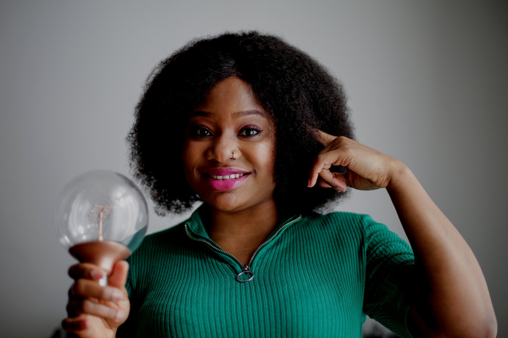 Positive young African American lady holding light bulb in hand on gray background